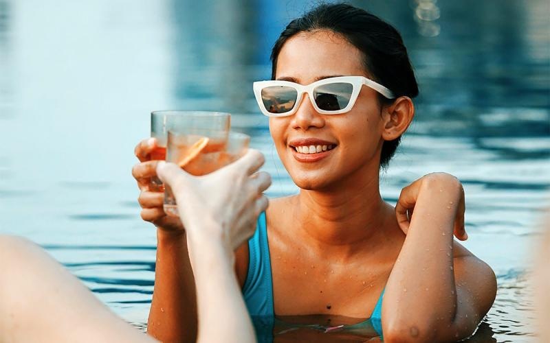 a woman in a pool holding a drink and a glass