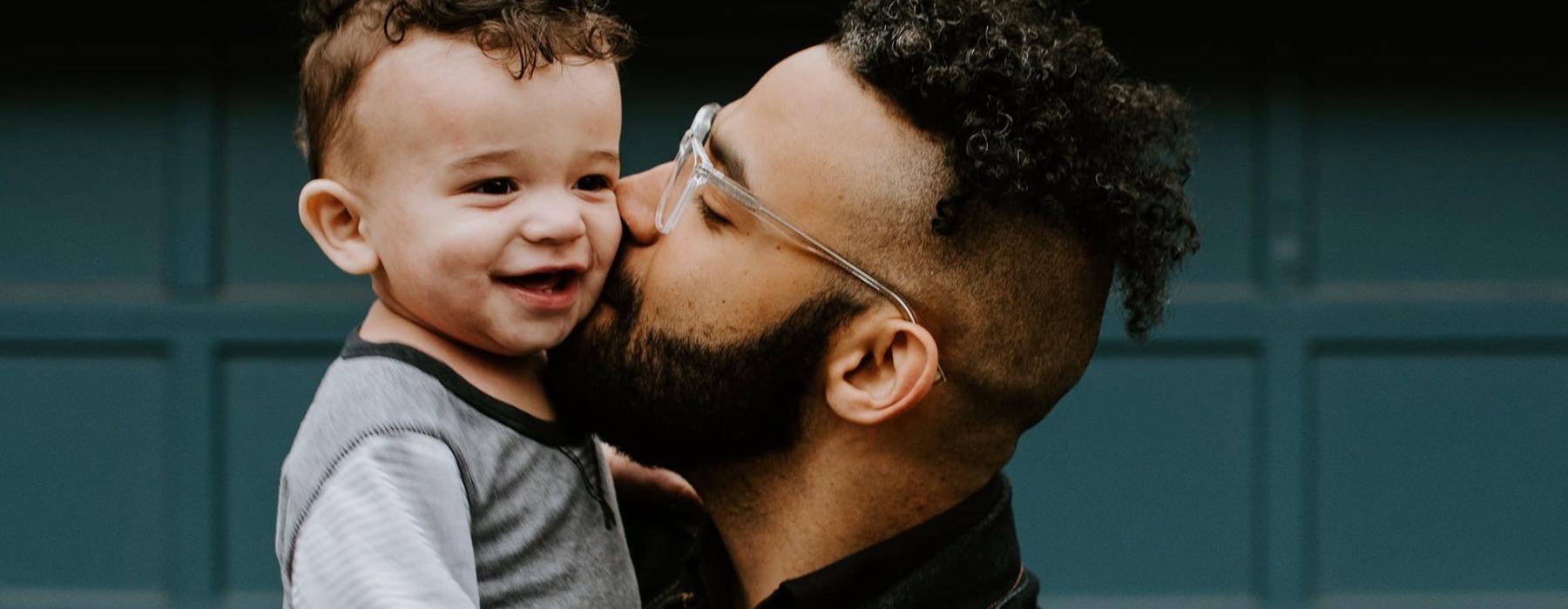 father holds and kisses his toddler son