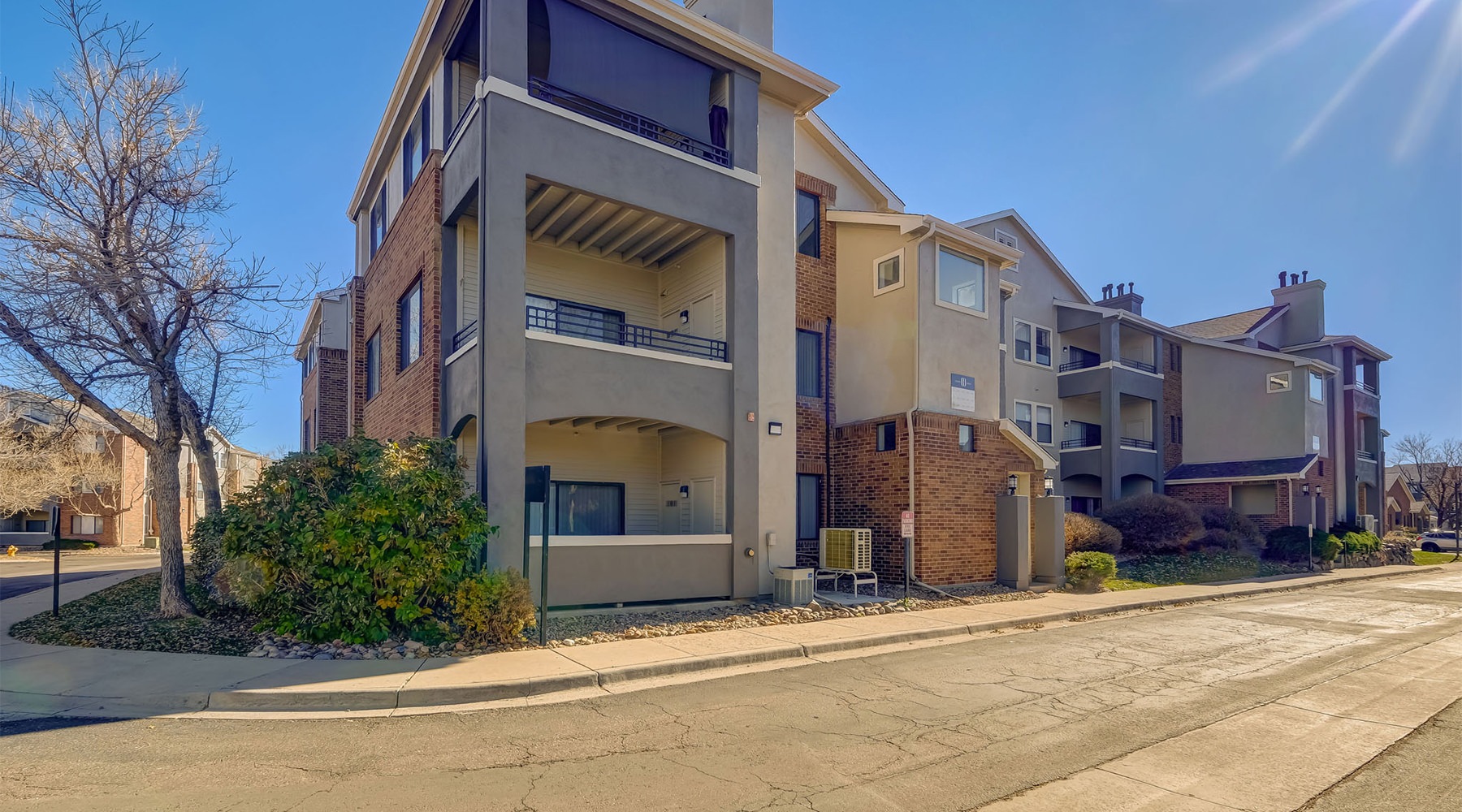 The essence of exceptional living A multi-story building at Cierra Crest Apartments features balconies and neutral tones, set along a street with a bare tree under a sunny sky.
